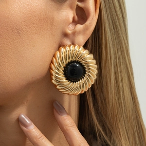 Boucles d'oreilles dorées avec texture spirale et pierre noire sur un modèle femme