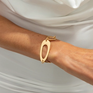 Gros plan d'un bracelet à gros maillons ovales dorés porté sur une manche blanche plissée