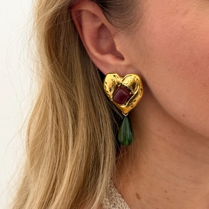 Nahaufnahme von goldenen Vintage-Herzohrsteckern mit grünem Harztropfen am Ohr des Models