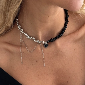 Detailaufnahme der asymmetrischen Halskette mit schwarzem Herzanhänger und Quasten