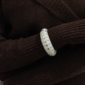 Close-up of creamy resin wide bangle with gold stud accents over brown knit sleeve