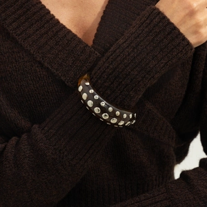 Close-up of wide amber resin bangle with silver rivets on brown knit sweater