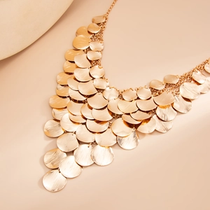 Detail of gold-tone metal discs with brushed texture on a multi-layer tassel necklace
