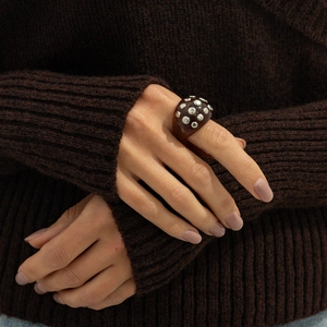 Close-up of a brown resin ring with silver studs worn over a knitted sweater