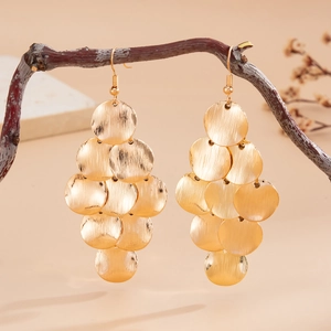 Close-up of golden leaf-shaped earrings hanging on branches with a warm background