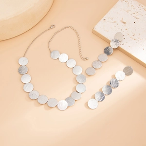 Minimalist silver brushed metal disc necklace and earring set on textured stone backdrop