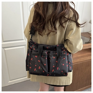 Close-up of black nylon crossbody tote bag with red cherry patterns and multi-pocket detail