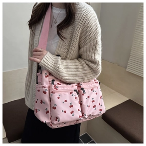 Pink shoulder bag with cherry print showing functional front zipper pockets and strap