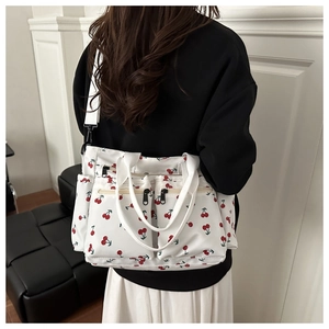 Detail of white canvas tote bag with red cherry patterns and adjustable shoulder strap