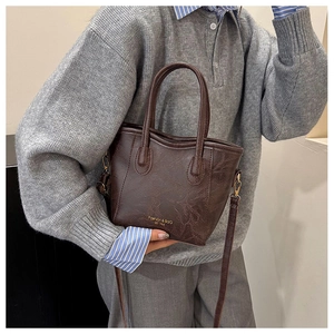Detail of dark brown marble texture leather bag with gold lettering and slim shoulder strap