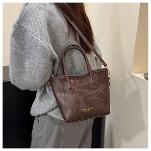 Detail of dark brown vintage leather tote bag with shoulder strap worn by a model