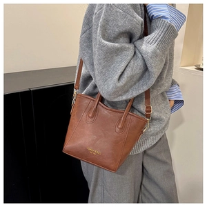 Close-up of brown leather bucket bag with top handle and adjustable strap worn by model