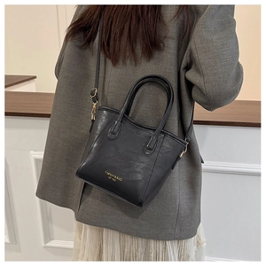 Detail view of a black leather bucket bag styled with a grey blazer and white skirt