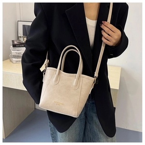 Detail of minimalist beige bucket bag held by a model in a stylish blazer outfit