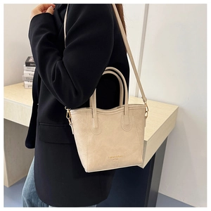 Detailed view of a beige minimalist bucket bag with gold lettering and slim shoulder strap