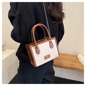 Detail of checkered beige tote bag with brown leather handles and a silver chain strap