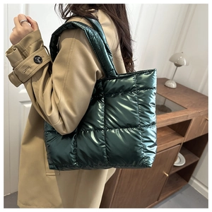 Sac fourre-tout matelassé vert foncé porté à l'épaule dans un décor minimaliste