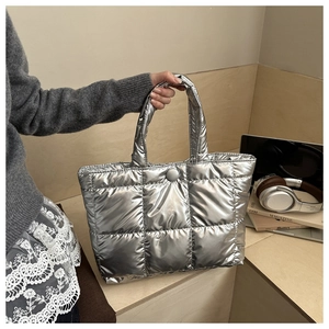 Détail d'un sac doudoune matelassé argenté tenu dans un cadre de vie chaleureux