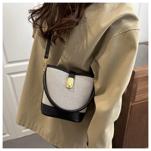Detail of canvas bucket bag with black leather trim and golden clasp on a model