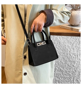 Close-up of matte black suede handbag with silver square turn-lock on beige trench coat