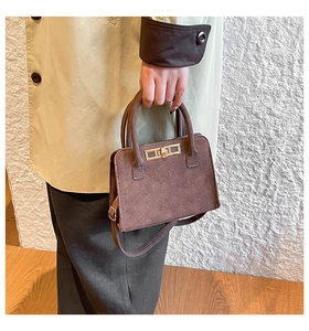 Detail view of dark brown suede handbag featuring a gold twist-lock and cylindrical handles