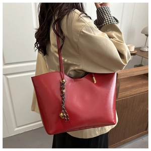 Macro detail of red oil wax leather tote bag with decorative woven pendant and metal bell