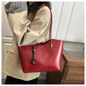 Detailed view of glossy burgundy leather tote bag with elegant decorative woven pendant