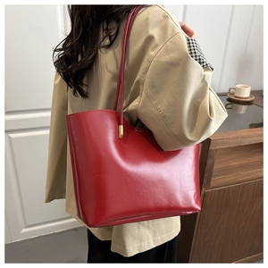 Close-up of red oil-wax leather tote bag on model shoulder with khaki trench coat