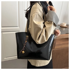 Detail of glossy black wax leather tote bag with braided gold bead charm on shoulder