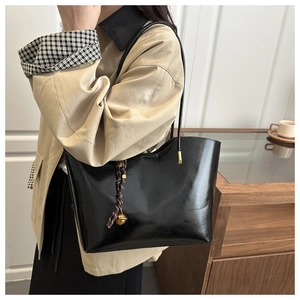 Macro detail of glossy black oil-wax leather tote bag with woven bell pendant charm