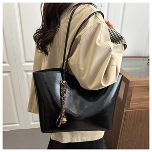 Detail view of large black tote bag with braided charm and golden metal ball accessory