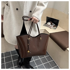 Macro detail of dark brown waxed leather tote with striped scarf and gold metal ball charm