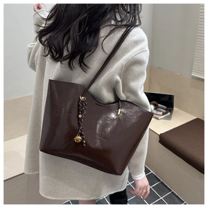 Detail of a dark brown oil-wax leather tote bag with a golden bell charm on the side