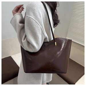 Detail of a large dark brown oil wax leather tote bag with shiny finish and gold hardware