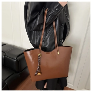 Detailed view of a vintage brown tote bag styled with a leather jacket and metal charm