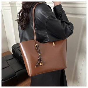 Brown oil wax leather tote bag with elegant weave tassel and gold bell detail shown on shoulder