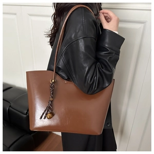 Brown oil-wax leather tote bag detail with braided rope and gold ball pendant