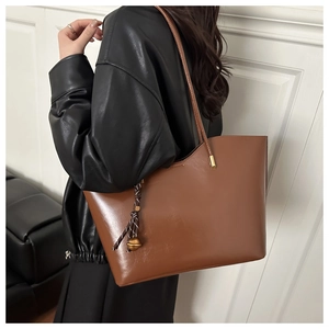 Close-up of a brown leather tote bag with a decorative woven knot charm on a model