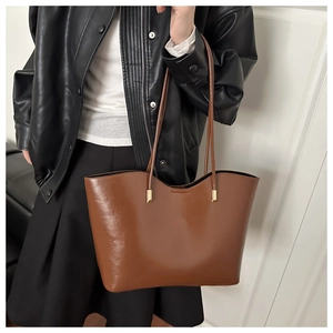 Close-up of a large brown leather tote bag with elegant gold hardware on a shoulder strap