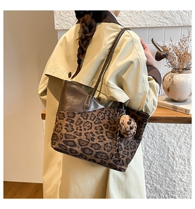 Detail of leopard print tote bag with plush ball charm and dark brown paneling on shoulder