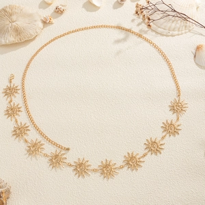 Detail of gold sun charms on bohemian metal body chain with sand and seashell background