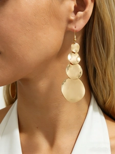 Detail of gold tiered circular disc drop earrings with brushed metal texture on a model