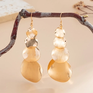 Close-up of golden geometric earrings with irregular metal discs on a branch