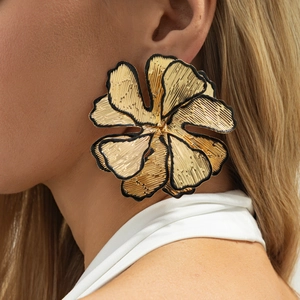 Close-up of large gold flower earrings with black enamel edges and hammered metal texture