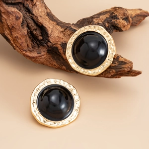 Detail of vintage round black enamel earrings with hammered gold metal edges on wood