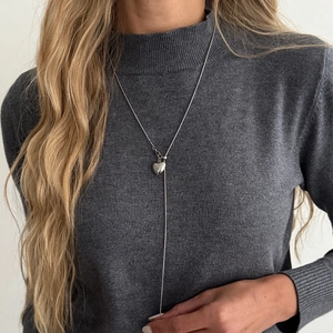 Lange zilveren ketting met hartjeshanger op een grijze trui voor een minimalistische look