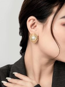Detailed close-up of a large pearl stud earring with golden spiral wire wrap on model