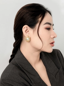 Detail shot of a large pearl stud earring with golden spiral design on model's ear