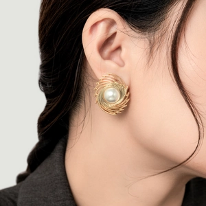 Elegant gold spiral stud earrings with large pearl on model for high-end fashion styling