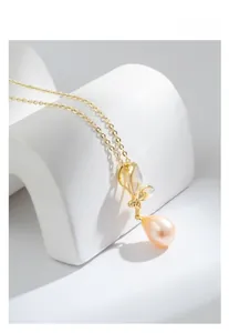 Détail du pendentif papillon doré avec nacre blanche et perle rose en forme de goutte